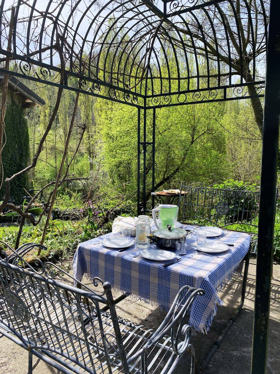 Vine-covered iron gazebo with a table set for lunch