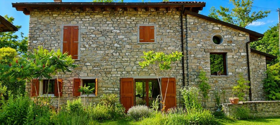 The stone facade of Ca'Lamma with wooden shutters and flowering garden